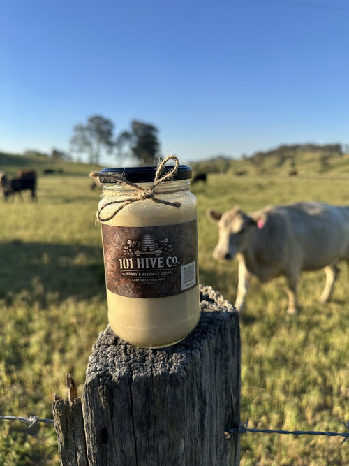101 Hive Co. Peanut Butter Honey 500g jar on a rustic fence post with cattle grazing in the background